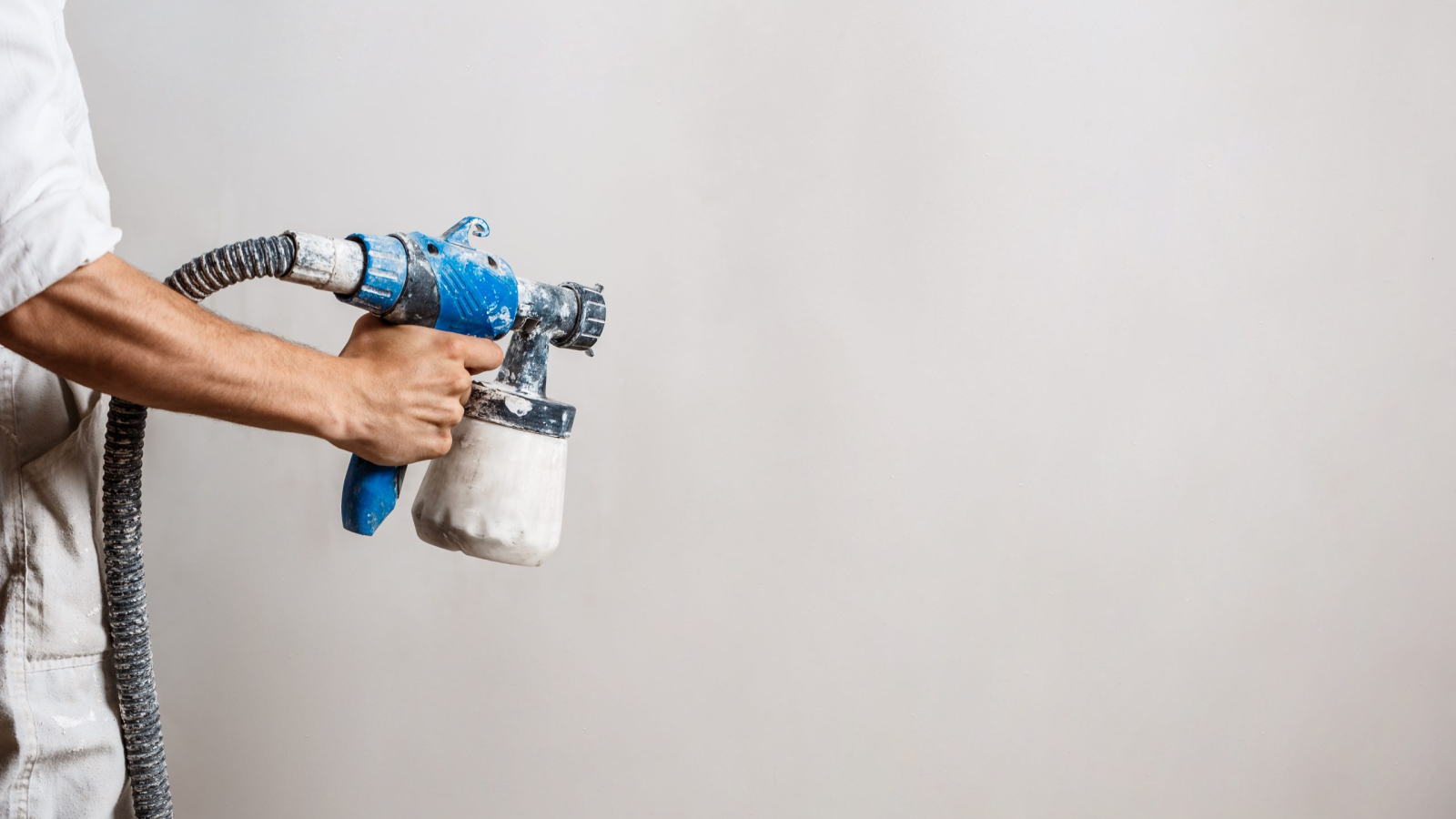 Worker painting wall with spray gun in white color. Copy space.