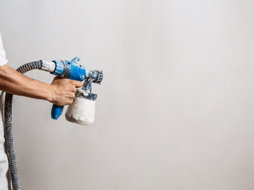 Worker painting wall with spray gun in white color. Copy space.